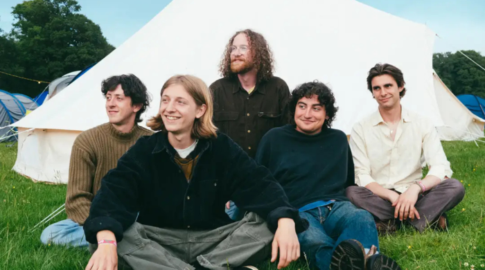Band looking happy in front of a tent whilst touching grass